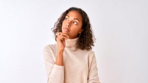 Young woman with hand on chin thinking about question, pensive expression.