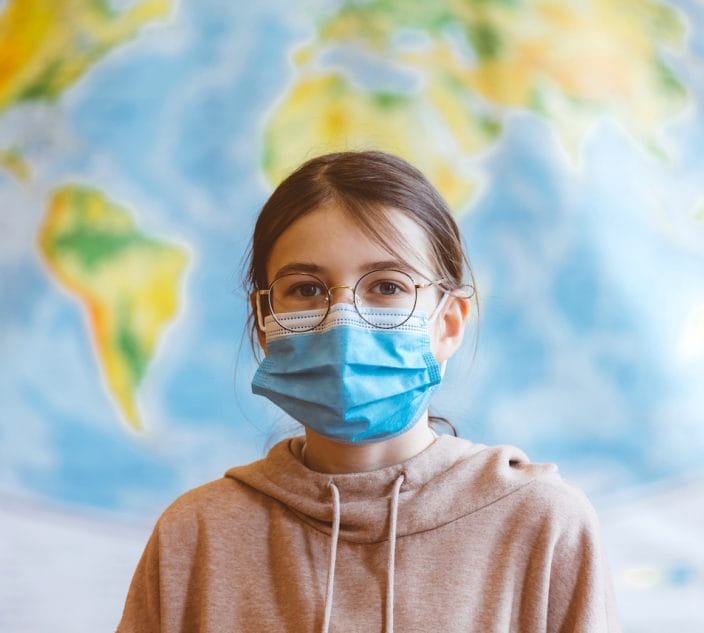 A 11-year-old teenager wearing a N95 Face masks is standing in front of a world map