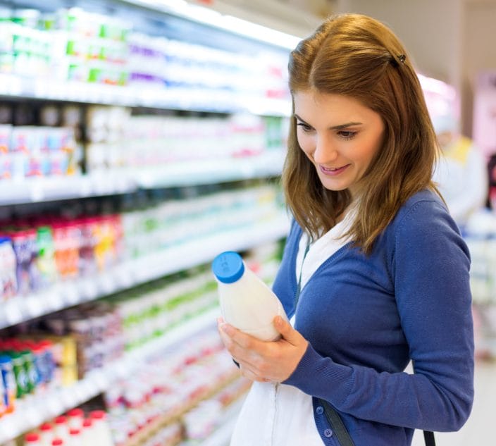 Young woman checking milk's labeling in supermarket.